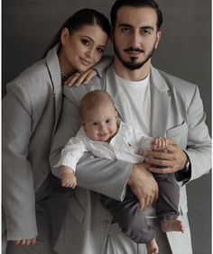 a man and woman holding a baby in front of a gray background with the caption's name on it