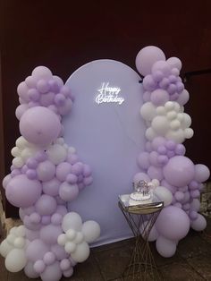 balloon arch with happy birthday sign and cake on small table in front of purple backdrop