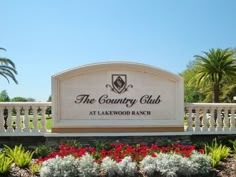 the country club at lakewood ranch sign surrounded by flowers and palm trees on a sunny day