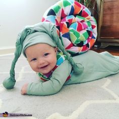 a baby is laying on the floor wearing a green outfit with a multicolored design