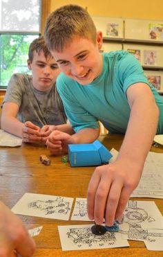 two boys sitting at a table playing with paper cut outs and stamping on them