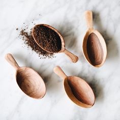 three wooden spoons filled with ground coffee on top of a white marble countertop