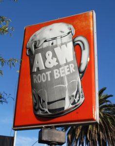 a large beer sign hanging from the side of a building next to a palm tree