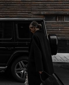 a woman walking down the street with her suitcase in hand and a black suv behind her