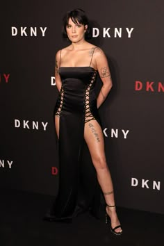 a woman in a black dress posing for the camera with her legs crossed and tattoos on