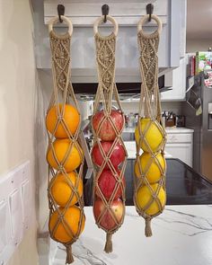 three hanging fruit baskets filled with apples, oranges and lemons on a kitchen counter