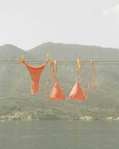 three bras hanging on a clothes line over the water with mountains in the background