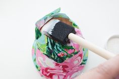 a hand holding a paintbrush over a flowered bag with a black brush in it