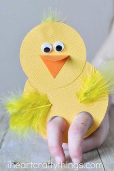 a child's hand holding up a yellow paper chick with feathers on its head