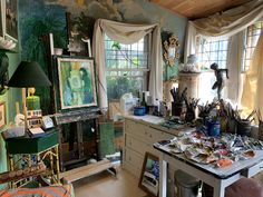 an artist's studio with lots of art supplies on the desk and in the window