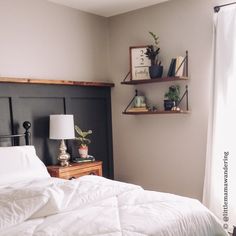 a bed with white comforter and pillows in a bedroom next to a wall mounted shelf