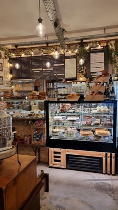 the inside of a bakery with lots of food on display and lights hanging from the ceiling