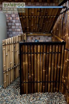 there is a small trash can in the middle of some bamboo fenced area with rocks and gravel around it