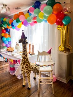 a giraffe standing in front of a table filled with balloons