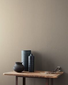 two vases are sitting on a wooden table in front of a green painted wall