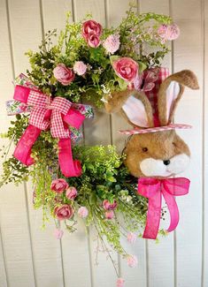 a wreath with pink flowers and a stuffed rabbit hanging on it's front door