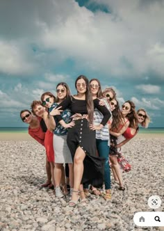 a group of women standing next to each other on top of a rocky beach with the ocean in the background