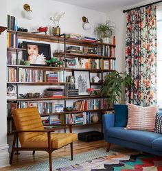 a living room filled with furniture and bookshelves next to a window covered in curtains