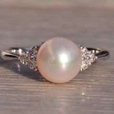 a pearl and diamond ring sitting on top of a wooden table