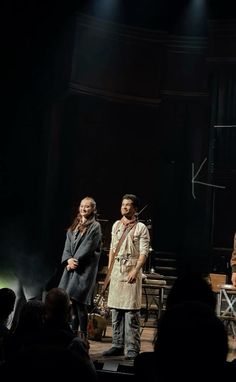 three people standing on stage in front of an audience at a musical performance with microphones