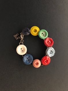 a bracelet made with buttons and chains on a black surface, the beads are multicolored