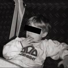 a black and white photo of a young boy sitting on a bus with his hand in his mouth