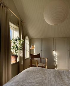 a bedroom with a bed, chair and potted plant on the window sill