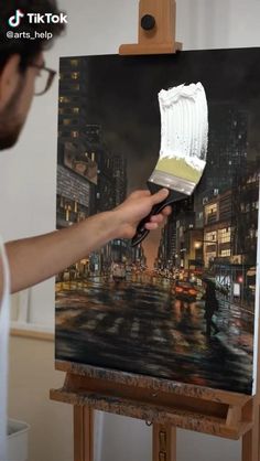 a person holding a paintbrush in front of an easel with a painting on it