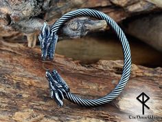 a close up of a metal bracelet on a wooden surface with a tree branch in the background