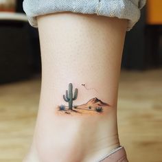 a small cactus tattoo on the side of a woman's leg, with mountains in the background