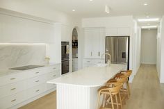 a kitchen with white cabinets and marble counter tops, along with bar stools that match the hardwood flooring