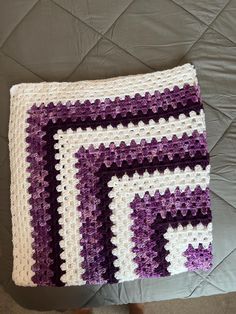 a purple and white crocheted blanket sitting on top of a bed