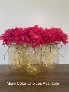 three mason jars filled with pink flowers and fairy lights are sitting on a wooden table