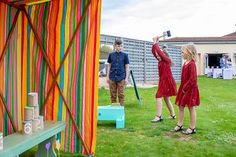 two women in red dresses are playing with baseball bats on the grass next to a colorful tent