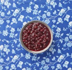 a metal bowl filled with cherries on top of a blue floral table cloth,