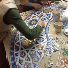 two women are working on mosaics at a table with cups and saucers in front of them