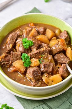 a green bowl filled with meat and potatoes on top of a table next to a spoon