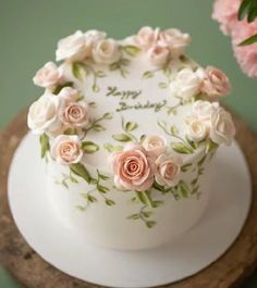 a white cake decorated with pink roses and the words happy birthday written on it in cursive writing