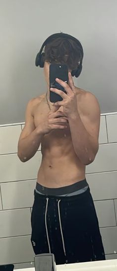 a shirtless man taking a selfie in the bathroom mirror with his headphones on