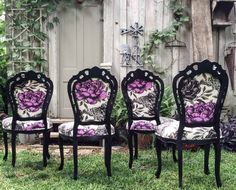 four black chairs with purple flowers on them sitting in the grass next to a fence