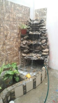 an outdoor fountain with rocks and water coming out of the top, in front of a brick wall