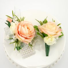 two boutonnieres on a white plate with pearls and flowers in the center