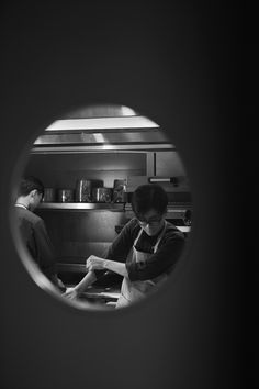 two people in a kitchen preparing food through a circular hole on the wall above them are pots and pans