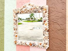 a mirror hanging on the side of a wall with seashells in front of it