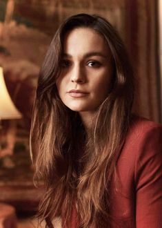 a woman with long brown hair sitting in front of a lamp and looking at the camera