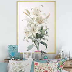 a vase with white flowers in it sitting on a bed next to two framed pictures