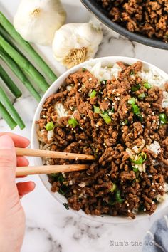 someone is holding chopsticks over a bowl of ground beef and onions with green onions