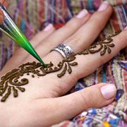 a woman with henna on her hand is using a green pen to draw something