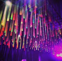 colorful lights hanging from the ceiling in a dark room with purple and green lighting behind them