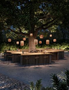 an outdoor dining area is lit up at night with paper lanterns hanging from the tree